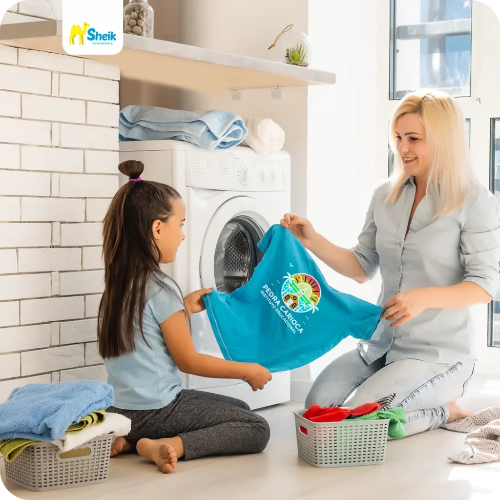 Mãe e filha sentadas no chão, segurando a camisa do uniforme escolar.